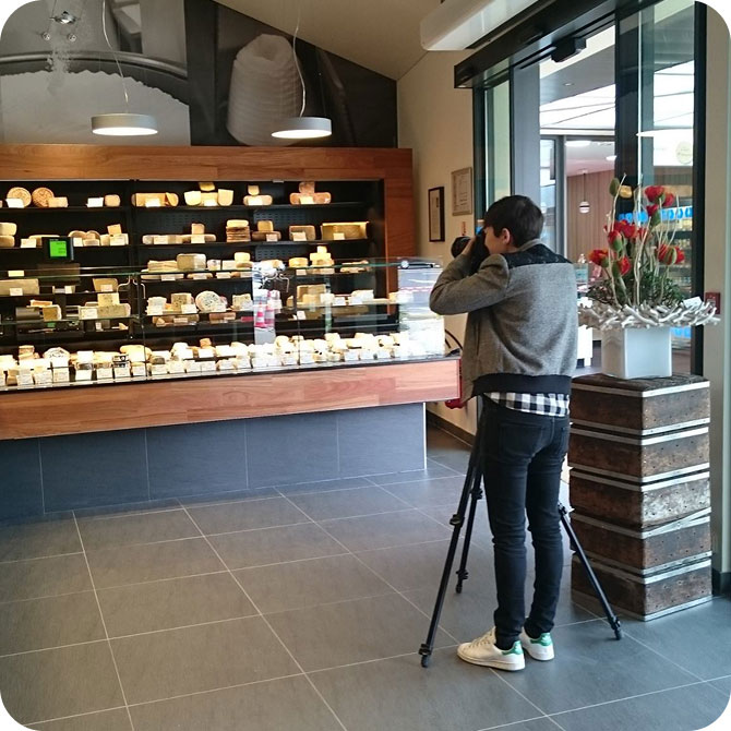 Jeune photographiant des fromages dans une fromagerie avec trépied
